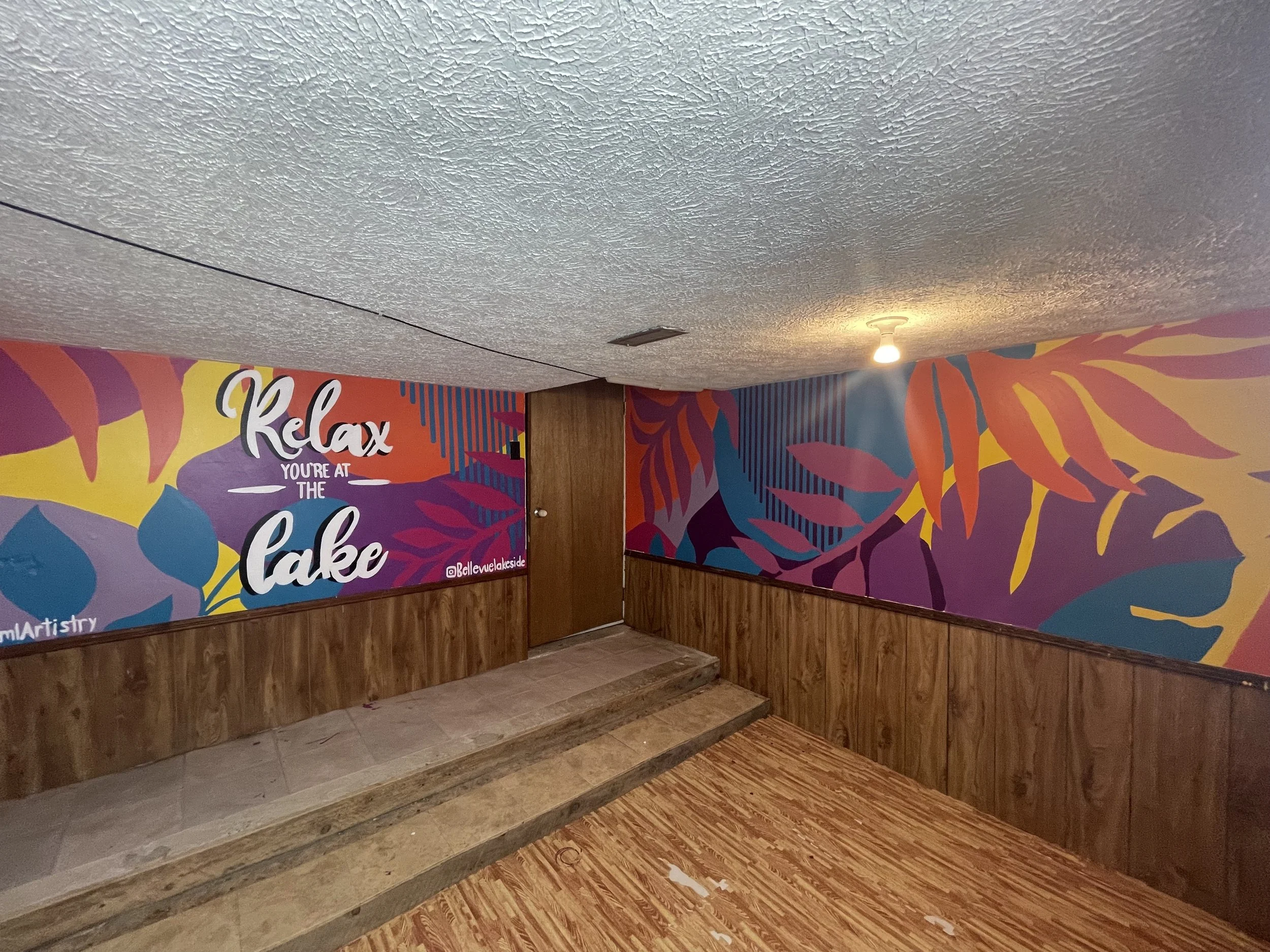 Colorful mural on a wall with tropical leaf designs and the words 'Relax you're at the Lake' written in white and black text.