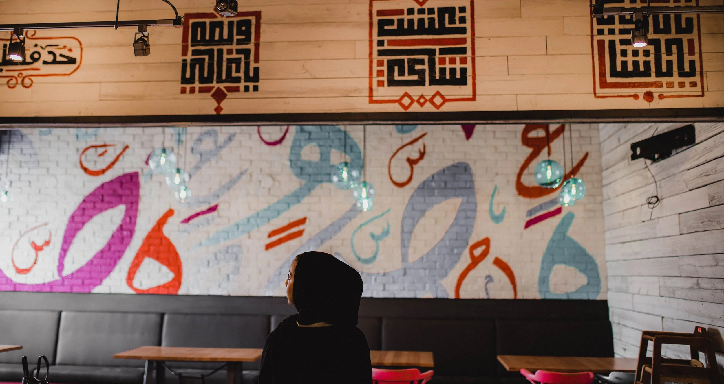 Interior of a restaurant or cafe with a woman wearing a black hijab sitting at a table.