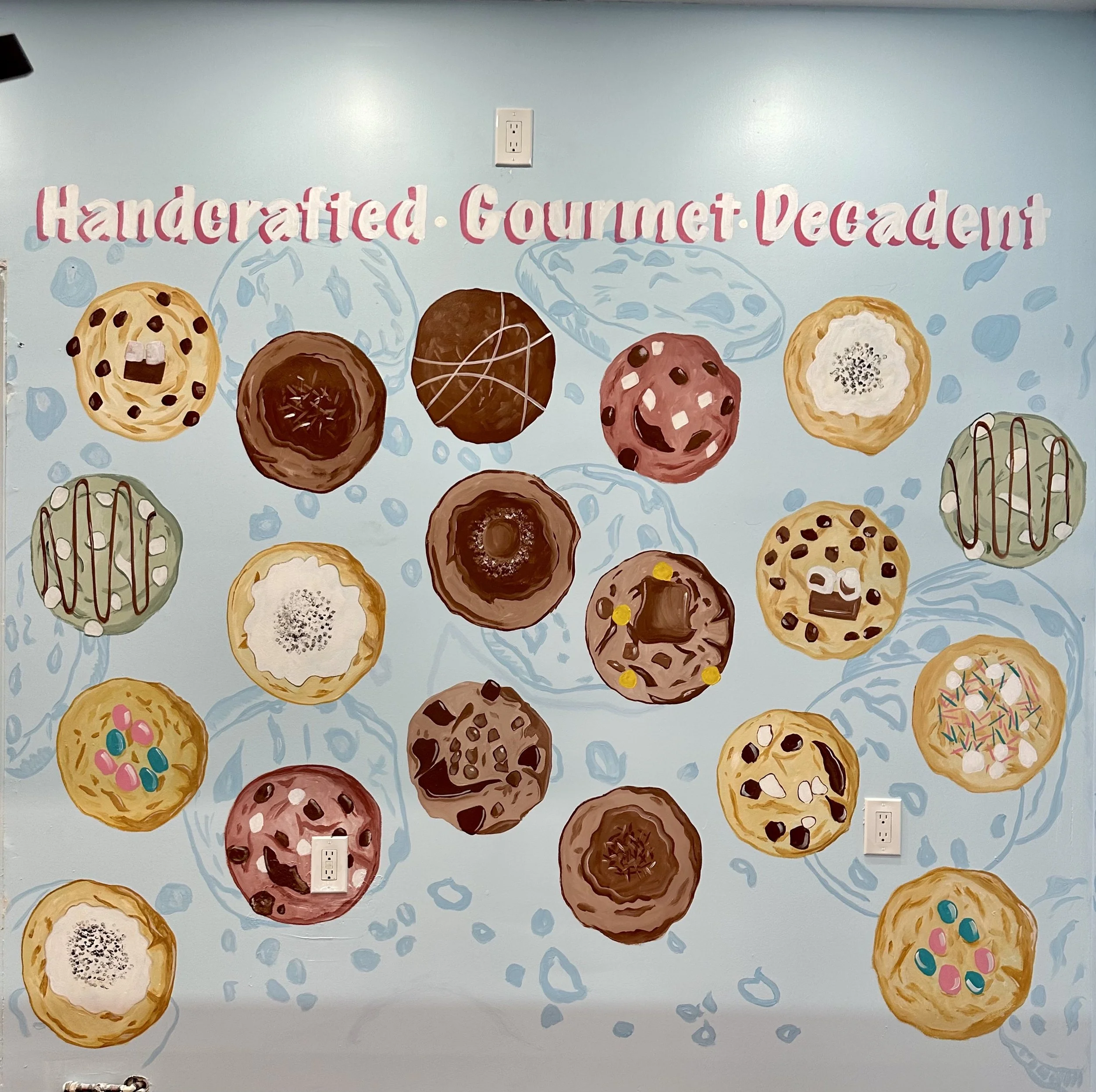 A colorful wall display of various decorated cookies with the words 'Handcrafted Gourmet Decadent' at the top.