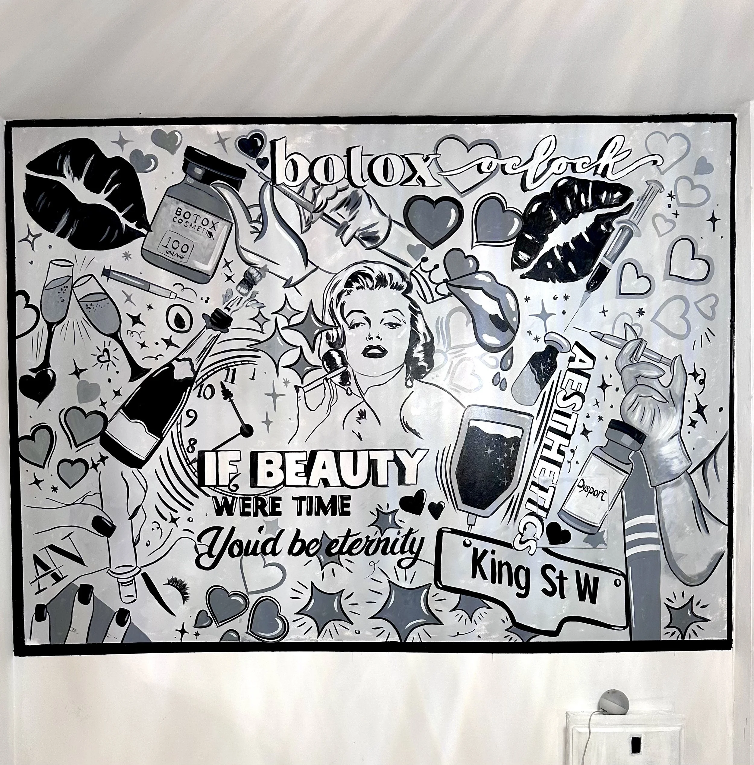 Black and white graphic mural advertising Botox and beauty products, featuring a vintage woman with a telephone, various cosmetic items like lips, syringes, and bottles, surrounded by hearts, stars, and clock motifs, with text including "beauty," "if