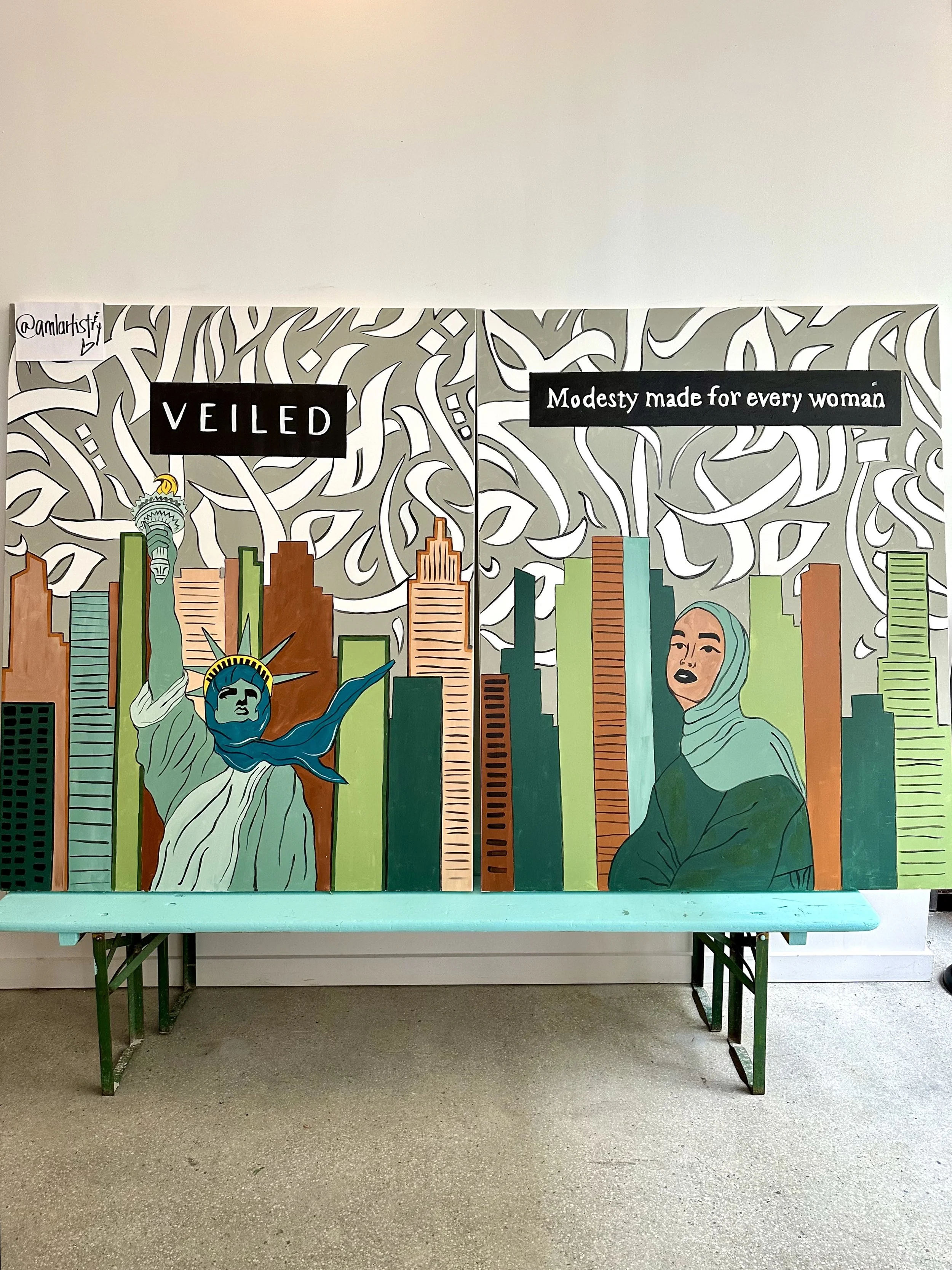A colorful painted mural with illustrations of the Statue of Liberty and a woman wearing a hijab, against a city skyline and a decorative white and gray patterned background. The mural includes black text boxes with white text reading 'VEILED' and 'M