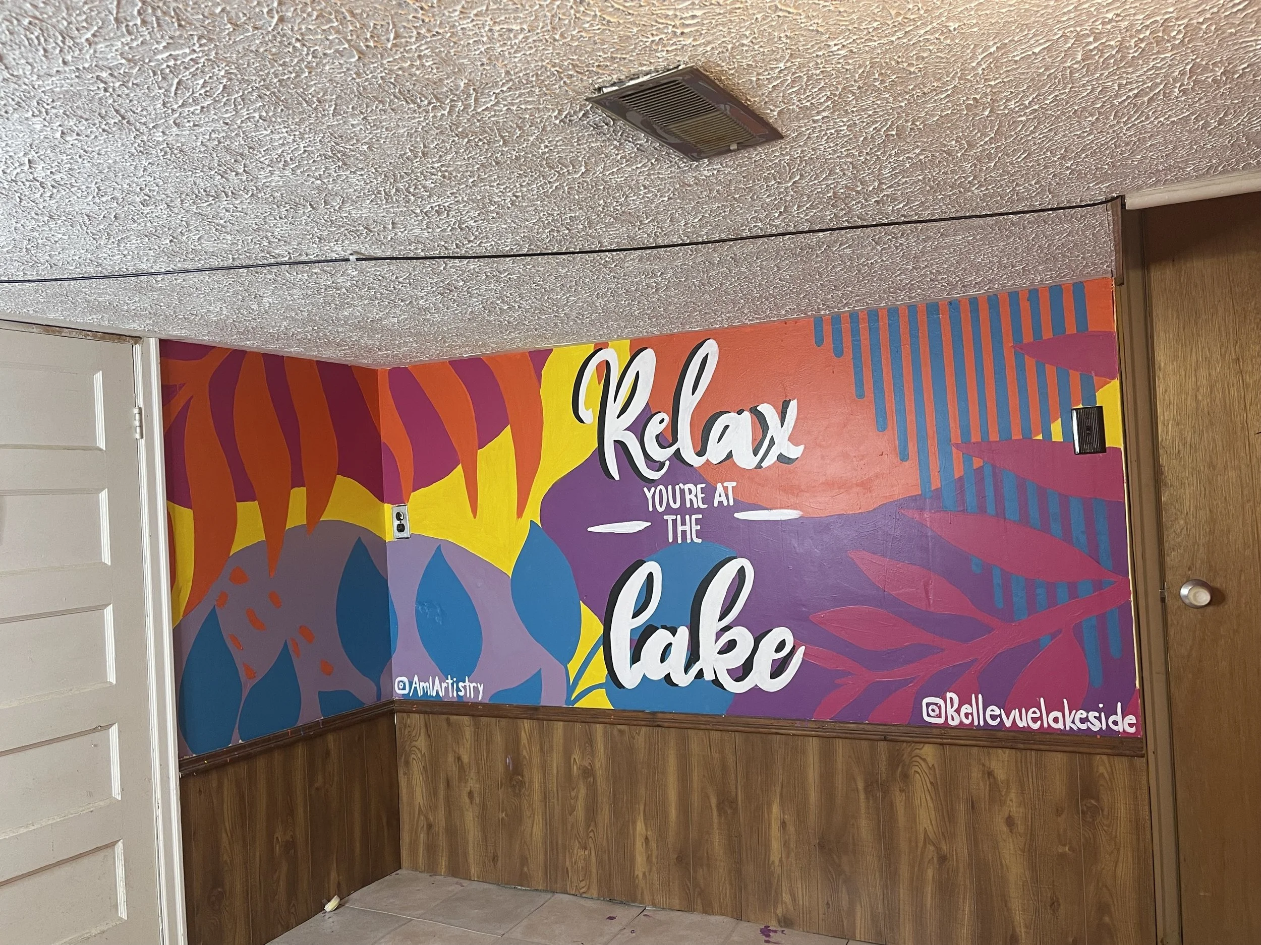 Colorful painted wall with the words 'Relax, You're at the Lake' and social media handles @AmiArtistry and @BellevueLakeside'
