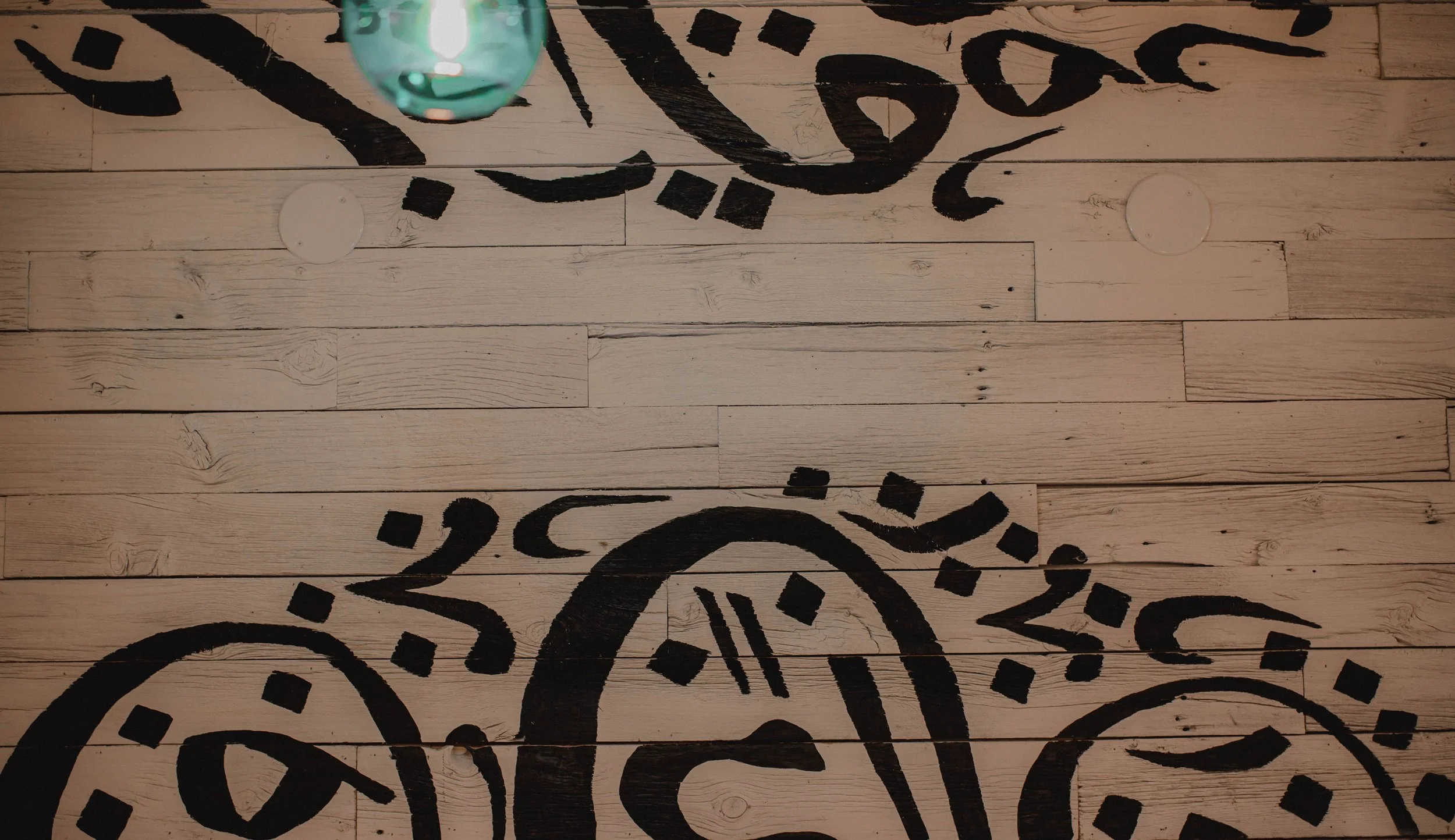 Close-up of a wooden floor with black abstract symbols or designs painted on it.