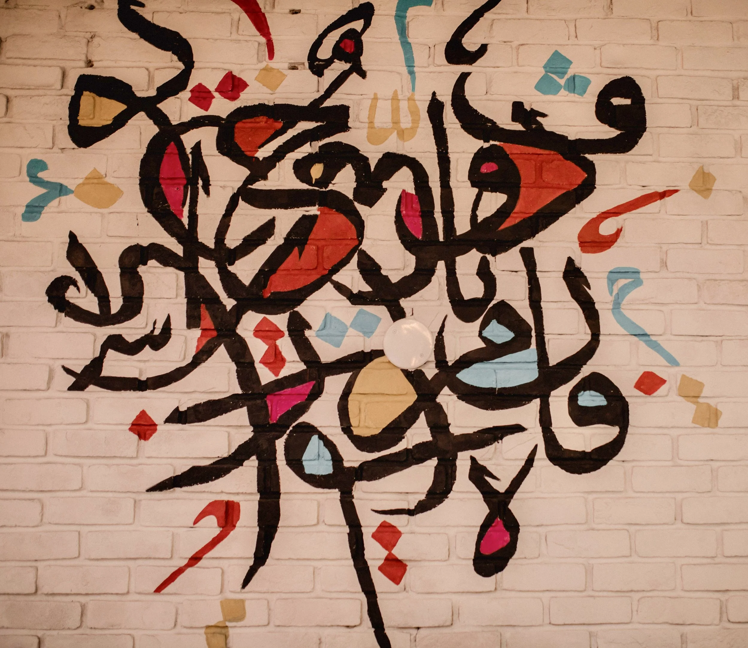 Abstract black graffiti-style art on a white brick wall with red, pink, blue, and tan accents.
