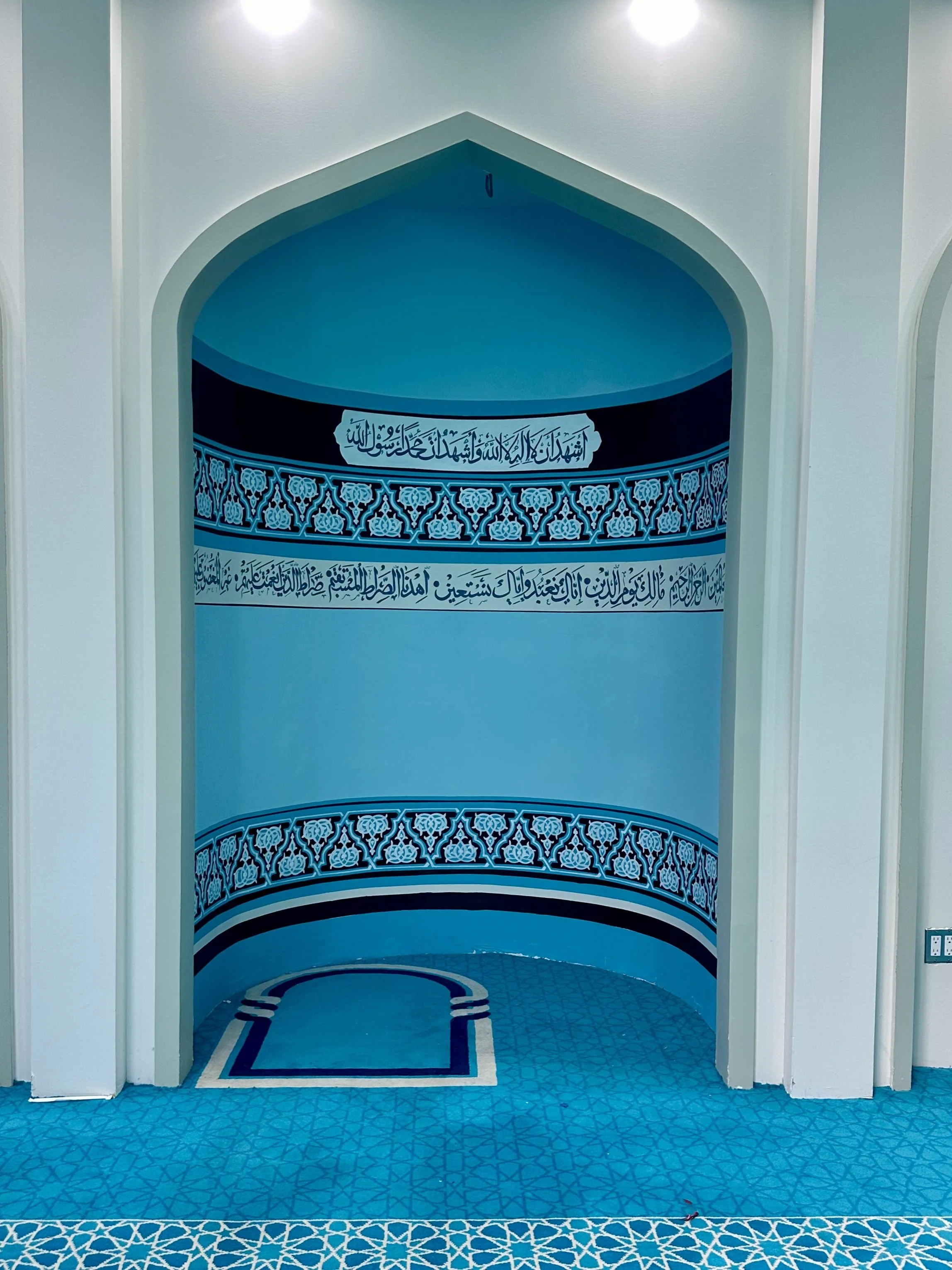 Interior of a mosque with Islamic calligraphy and decorative motifs in blue and white.